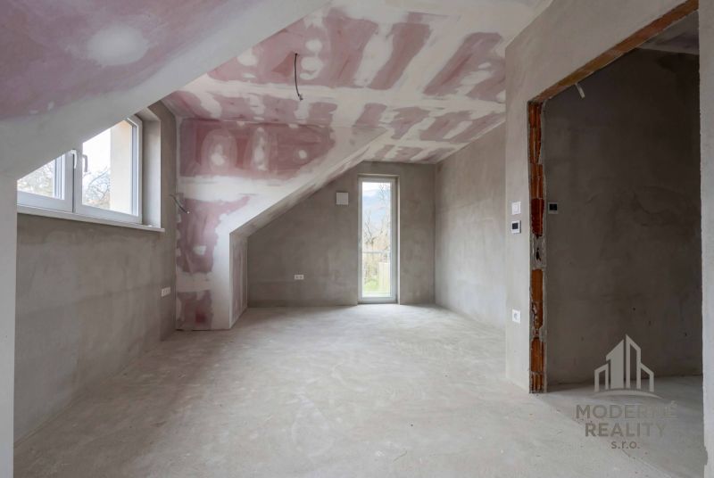 Attic room in a family house with a sloped ceiling, raw walls, and a window.
