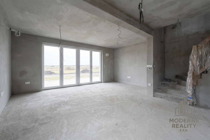 A spacious interior of a family house with large windows and a cement floor.
