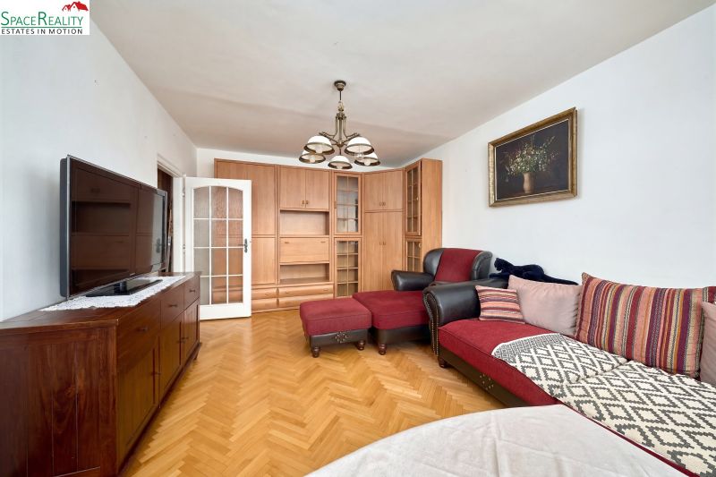 Living room in a two-room apartment with a red sofa, TV, and wooden decor flooring.