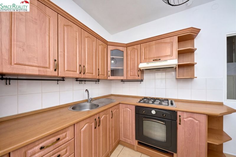 Corner kitchen with wooden cabinets, stovetop, and extractor hood in a two-room apartment.