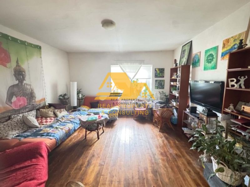 Living room of a family house with Buddha decorations, a sofa bed, and a wooden-patterned floor.