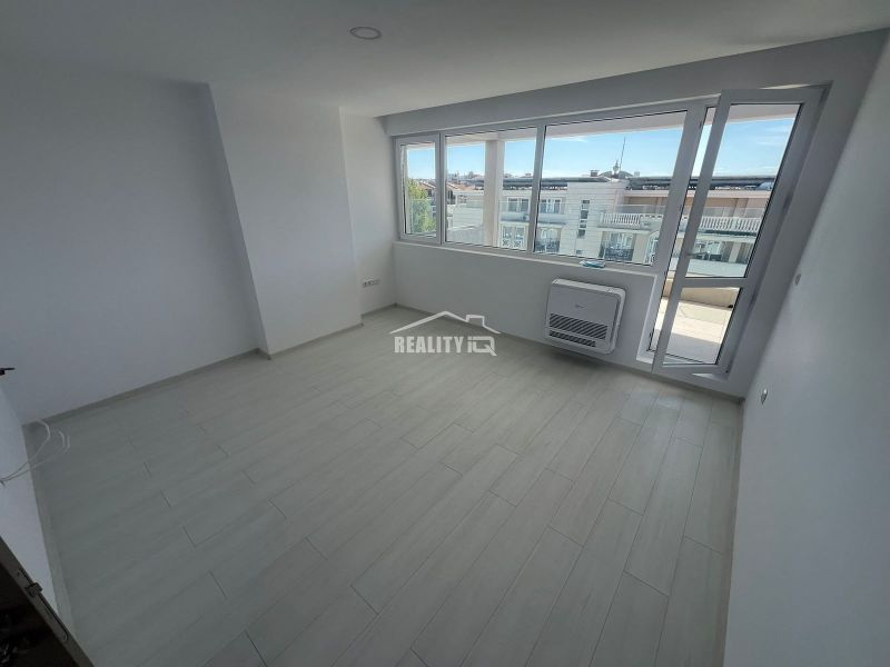 A bright room in a 2-bedroom apartment with wood-patterned flooring and large windows.