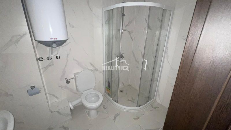 Bathroom with toilet and shower in a 2-room apartment, white tiles.