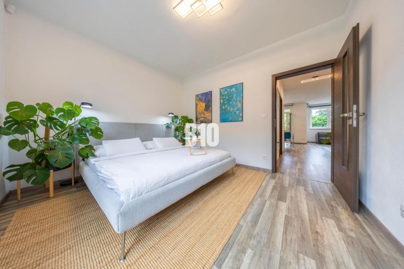 A bright bedroom with a plant, wooden floor decor, and art on the wall in a 3-room apartment.