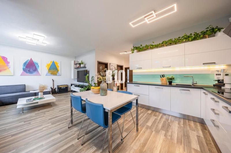 A kitchen in a 3-room apartment with a wooden decor floor, light furniture, and houseplants.