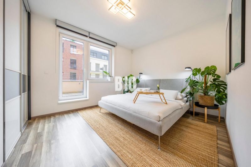 A bright bedroom in a three-room apartment with a bed, plants, and a wooden decor floor.