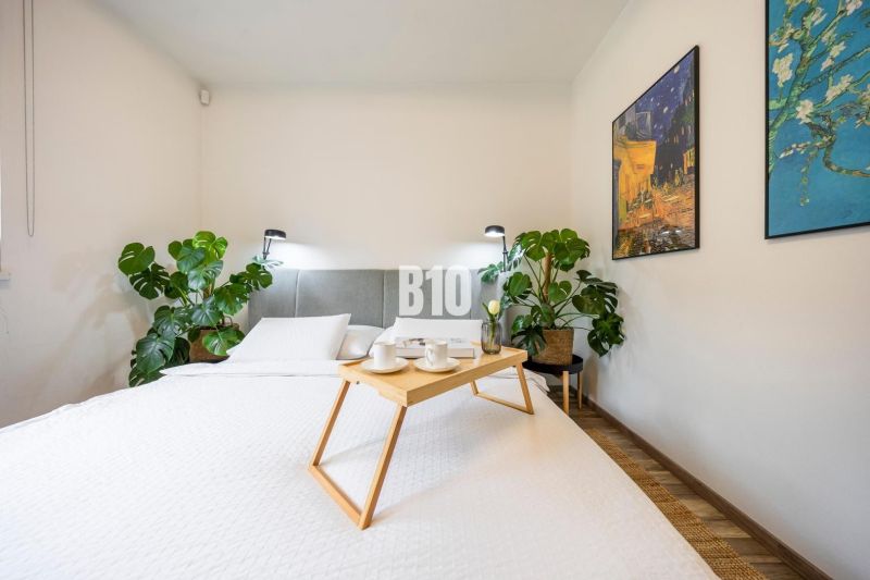 A bright bedroom in a 3-room apartment with a bed, plants, and paintings on the wall.