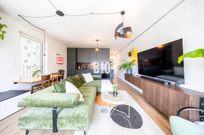 Living room in a three-room apartment with a wooden decor floor, a green sofa, and a television.