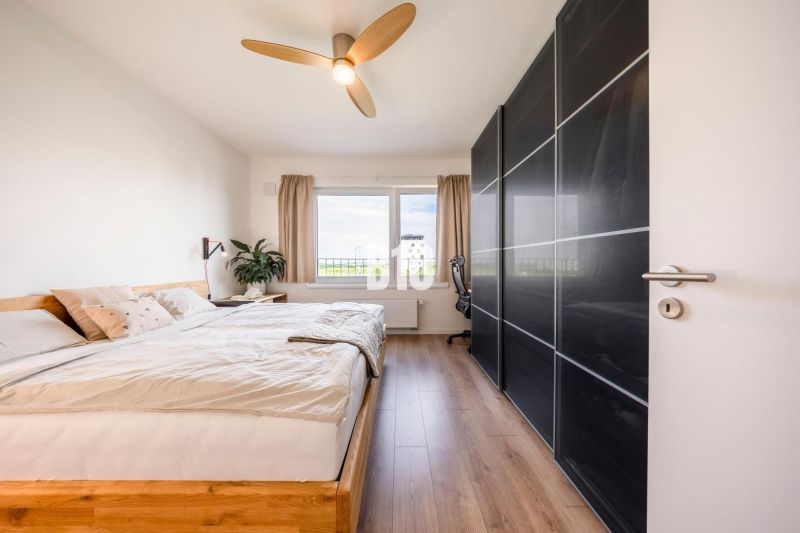 A bright bedroom with a large bed, wood-patterned flooring, and a wardrobe.