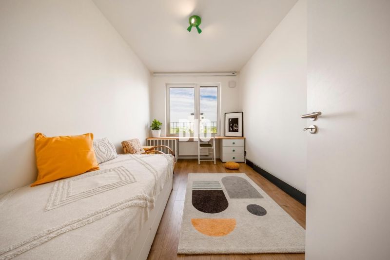 A room in a 3-room apartment with a bed, a table, a floor with a wooden decor, and a colorful carpet.