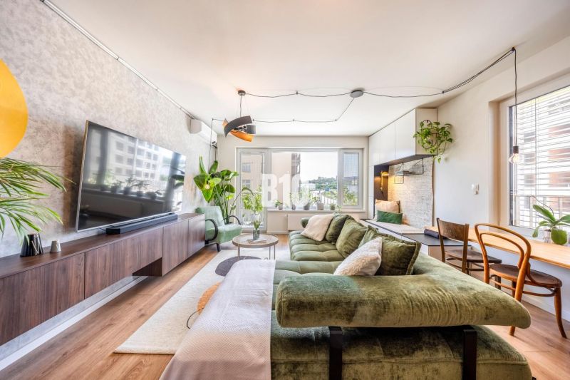 Living room in a 3-room apartment with a comfortable green sofa, a large television, and plants.