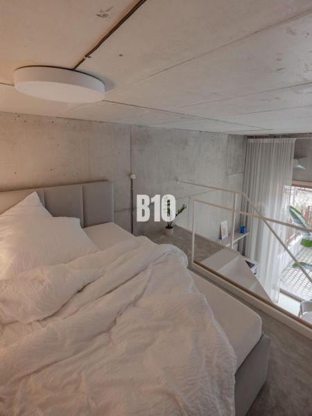 Loft bedroom with a concrete ceiling in a 2-room apartment, with white bed linen.