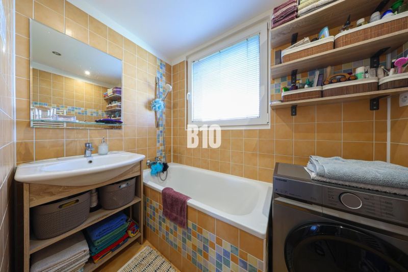 A bathroom in a 3-room apartment with a bathtub, washing machine, sink, and storage shelves.