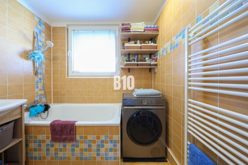 A bathroom in a 3-room apartment with a washing machine, a bathtub, and orange tiles.