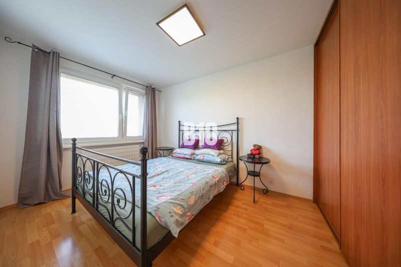 A bedroom with a bed, a cabinet, and a wooden decor floor in a three-room apartment.