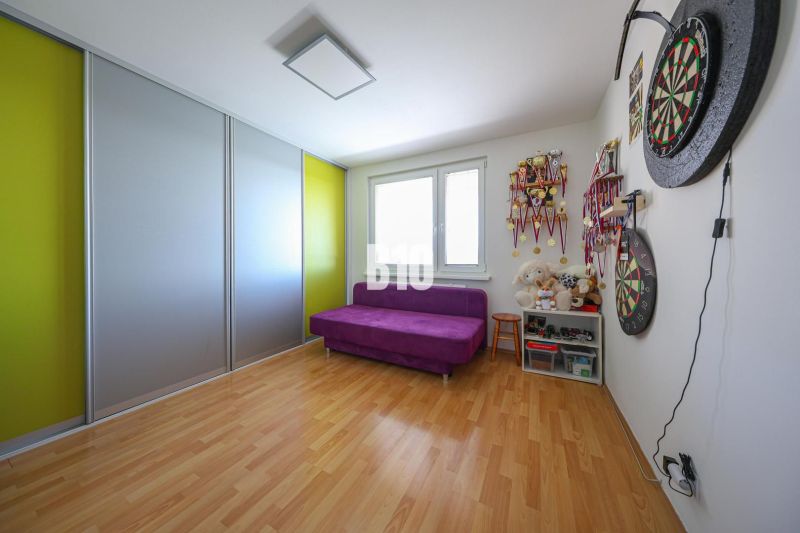 A room with a purple sofa, a wooden-patterned floor, and a shelf with medals in a three-room apartment.