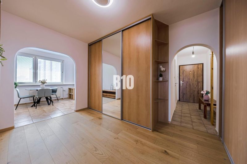 Interior of a 3-room apartment with a wooden decor floor, mirrored wardrobe, and dining area.