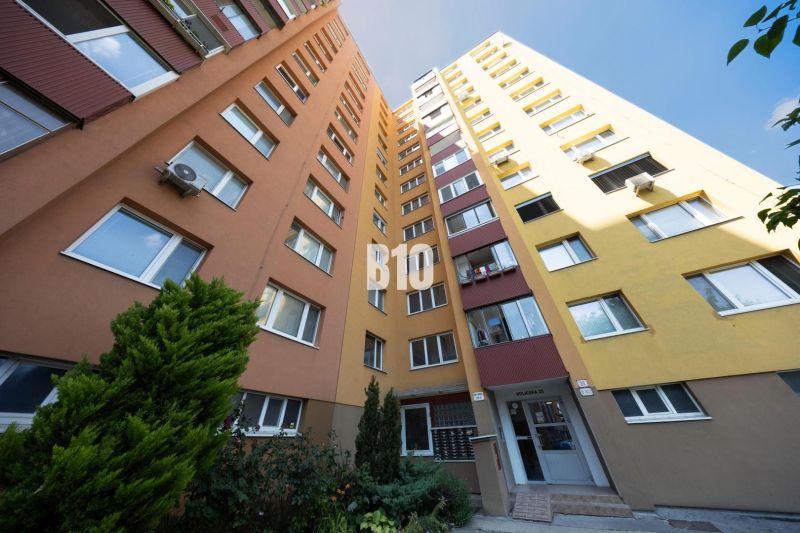 Apartment building in Bratislava V with an orange-yellow facade and greenery at the entrance.
