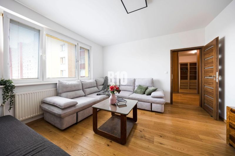 A bright living room with a corner sofa, wooden doors, and a floor with a wood decor.