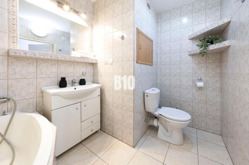 Bathroom with a bathtub, sink, mirror, toilet, and decorative shelves in a 3-room apartment.