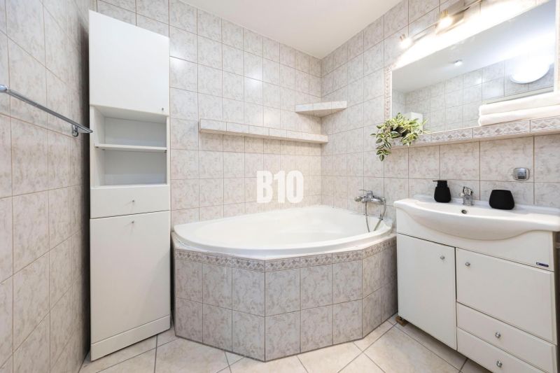 A bathroom with a bathtub, sink, and cabinets in a 3-room apartment with white tiles.