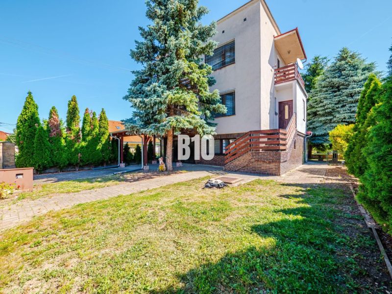 A family house in Branč with greenery, a terrace, and wooden details on the railing.