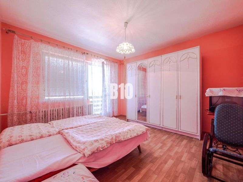 Bedroom with pink walls, a wardrobe, a bed, and a wooden decor floor in a family house.
