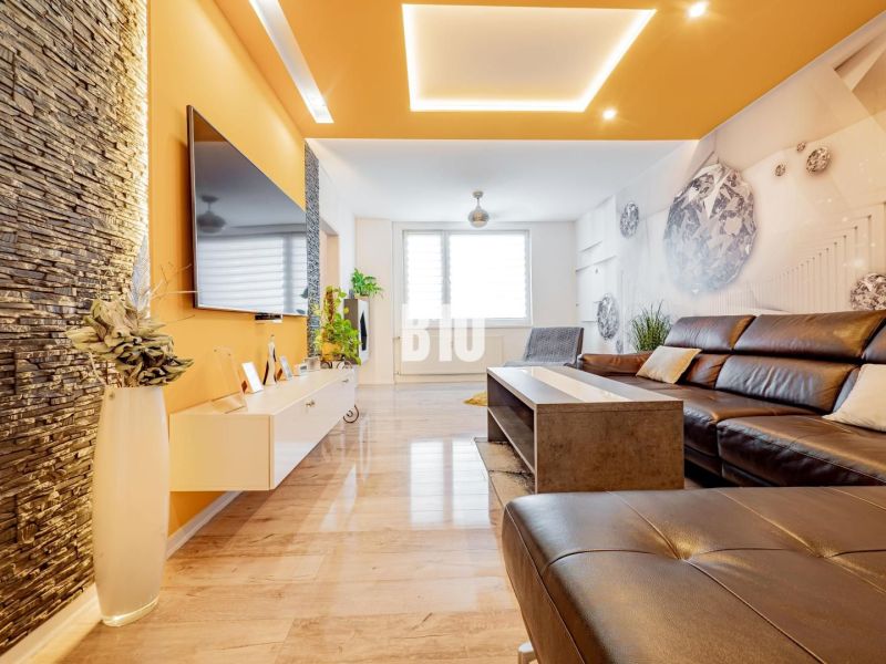 Living room of a three-room apartment with a fireplace, leather sofa, and wooden decor flooring.