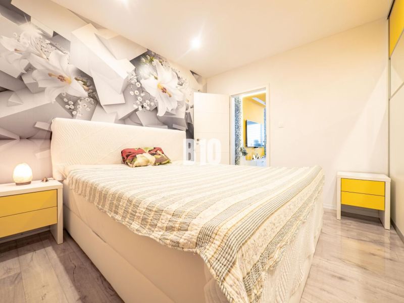 A bedroom in a 3-room apartment with floral wallpaper, yellow details, and a floor with a wooden decor.