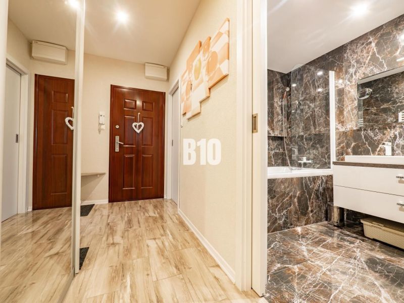 A hallway with a wooden decor floor leads to a luxurious marble bathroom in a 3-room apartment.