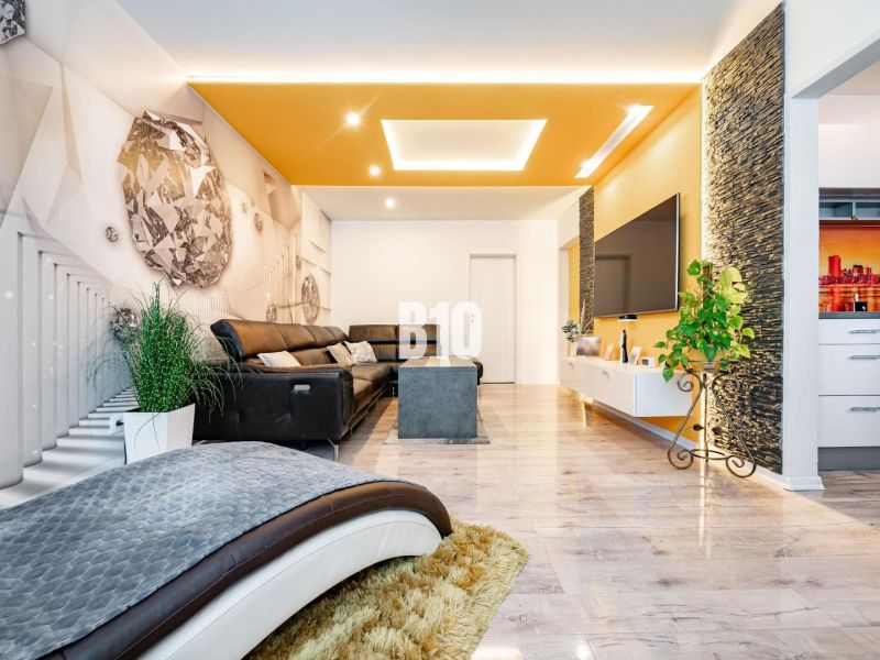Interior of a 3-room apartment with a sofa, large television, wall decor, and wood-patterned flooring.