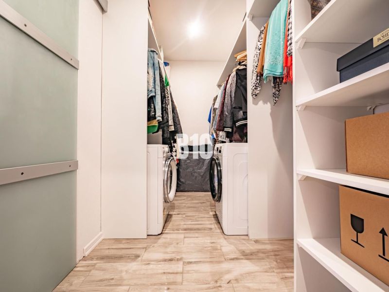 Wardrobe with a washing machine in a 3-room apartment, floor with wood decor, shelves and clothes.