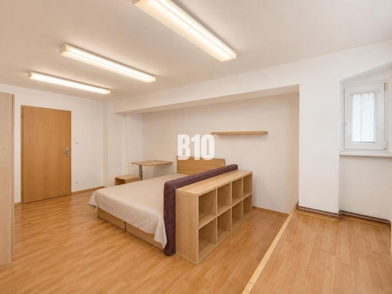A room in a 2-bedroom apartment with a bed and a floor with a wooden decor.