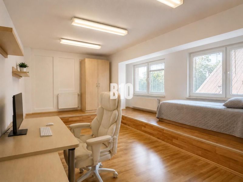 A spacious room in a 2-room apartment with a computer desk and a bed on an elevated floor.