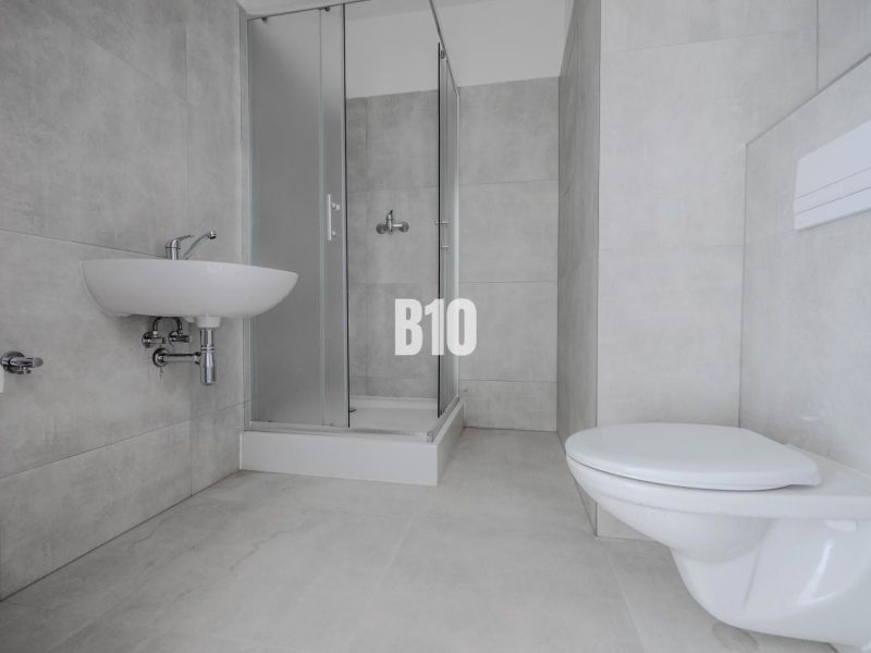Bathroom with a shower and light tiles in a studio apartment.