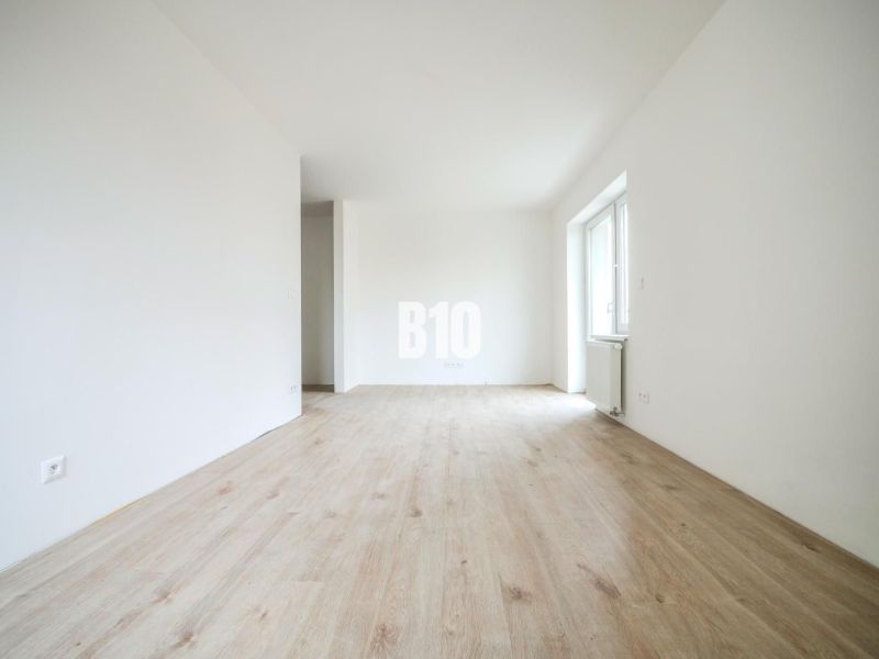 A bright interior of a one-room apartment with a wooden decor floor and white walls.