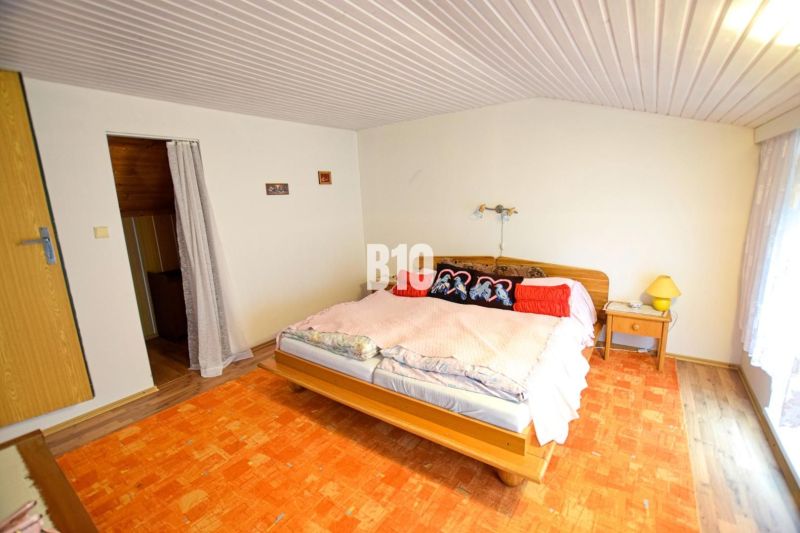 A bedroom in a cottage with a bed, decorative pillows, and an orange carpet.
