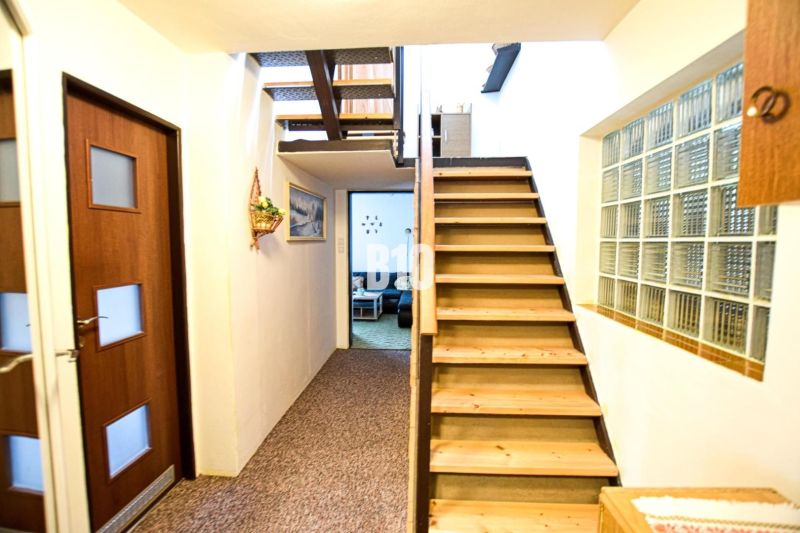 The interior of a cabin with a wooden staircase, doors, a glass block window, and a painting on the wall.