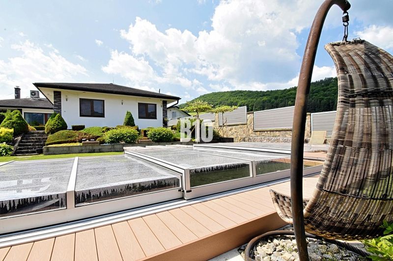 A family house in Súľov-Hradná with a covered swimming pool and a landscaped garden on a sunny terrace.