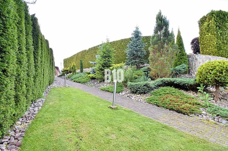 A landscaped garden of a family house in Súľov-Hradná with a path surrounded by greenery and ceramics.