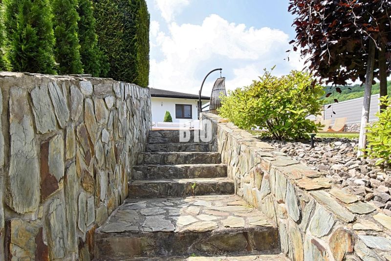 Stone steps leading to a family house in Súľov-Hradná surrounded by greenery and stones.