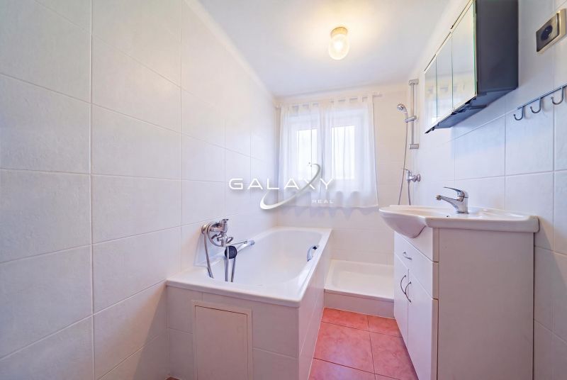 A bathroom in a family house with a shower, bathtub, sink, and a window with white curtains.