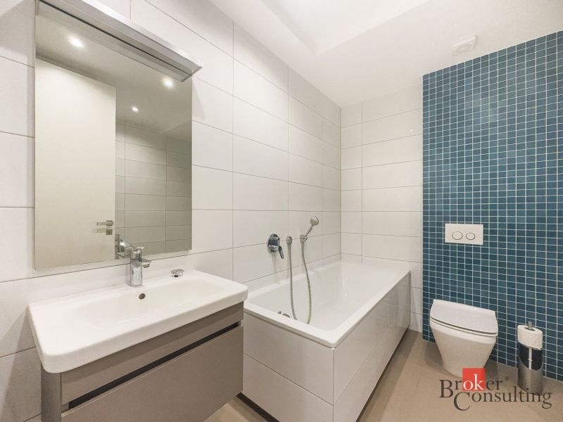 A bathroom of a 2-room apartment with a bathtub, sink, and toilet in white and blue tiles.