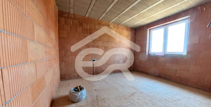 The interior of an unfinished room in a family house with a brick wall and a window.