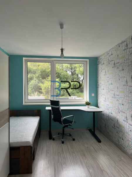 A room in a family house with a desk, a bed, and a floor with a wooden decor.