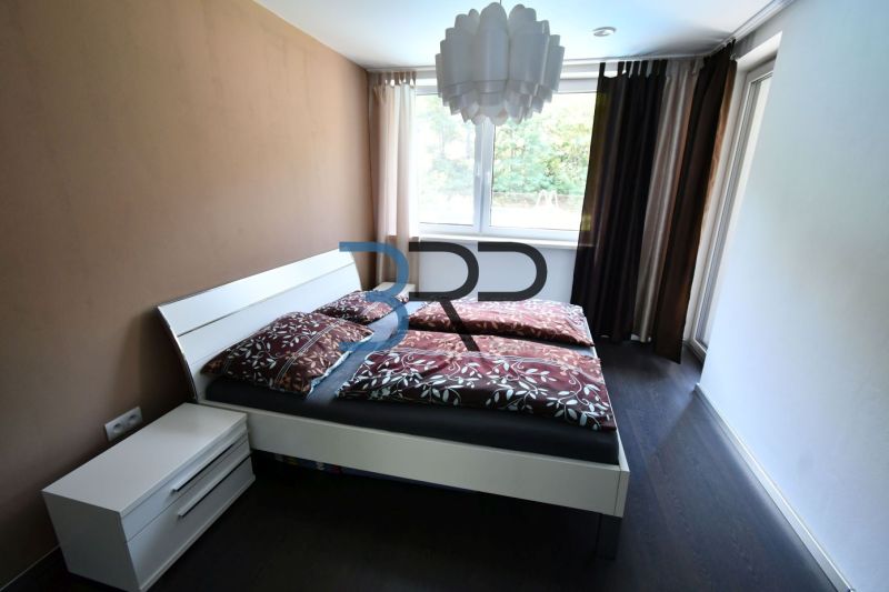 A bedroom with a light wall, a bed, and a wooden decor floor in a family house.