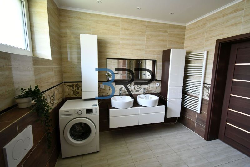 A bathroom with two sinks, a washing machine, and cabinets in a family house.