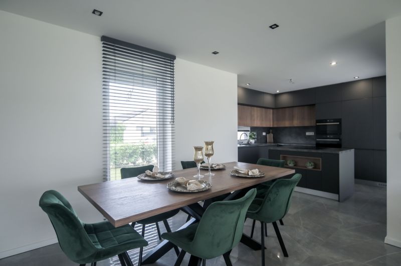 Dining room in a family house with a wooden table, green chairs, and a black kitchen.