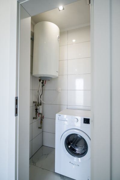 Washing machine and boiler in the bathroom of a family house, tiled with white tiles.