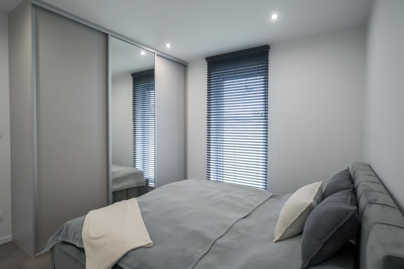 A bedroom in a family house with a large built-in wardrobe, a bed, and blinds.